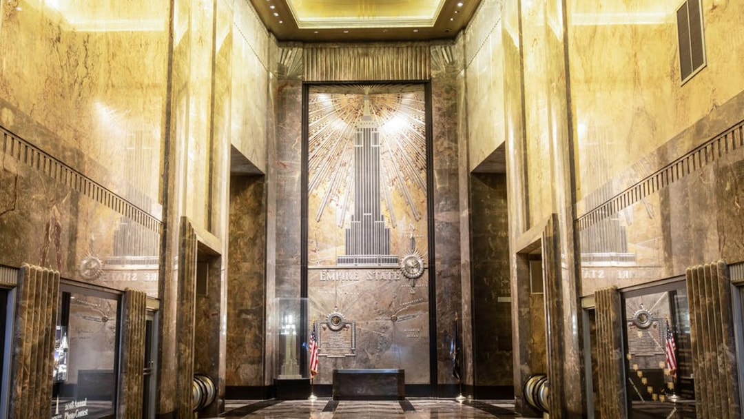Empire State Building Art Deco lobby with golden ceiling and mural.