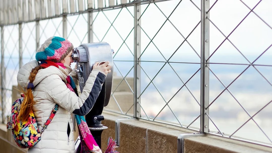 Visitor using binoculars on Empire State Building's 86th floor observatory.