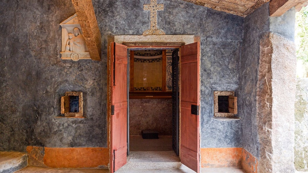 Convento dos Capuchos entrance with open wooden doors and stone cross above, Sintra, Portugal.