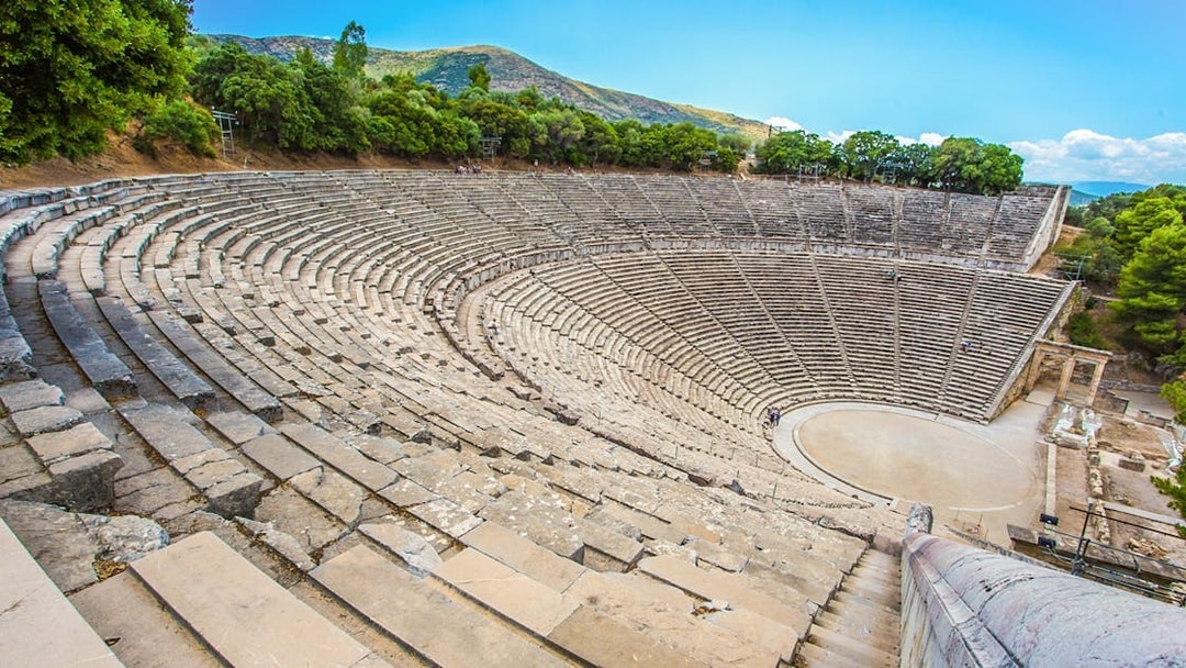 Epidaurus Ancient Theatre with stone seating and stage, surrounded by trees.