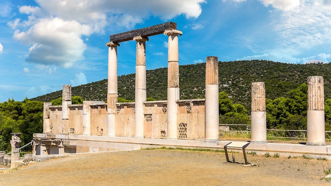 Ancient columns at Epidaurus Theatre, Greece, with scenic hillside backdrop.