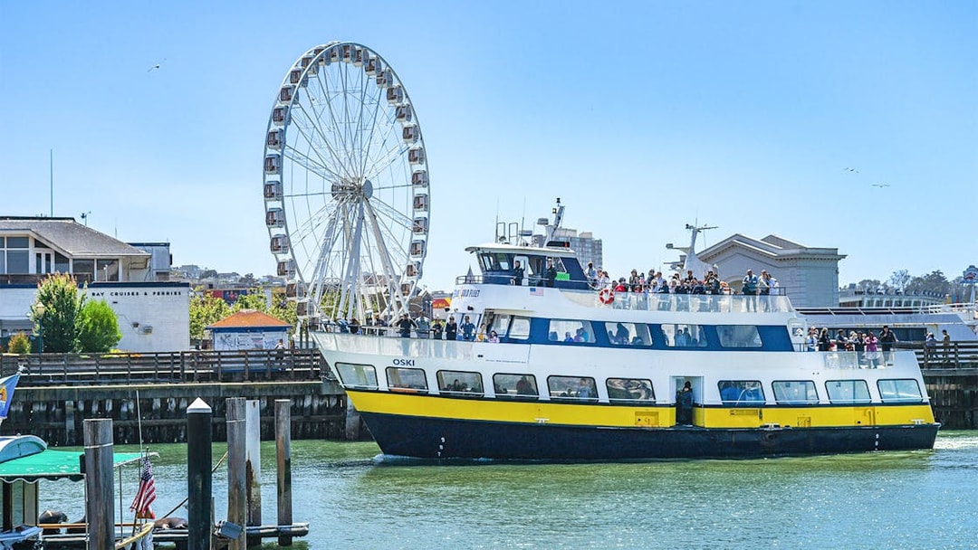 Ferry near San Francisco coast with Ferris wheel in background.