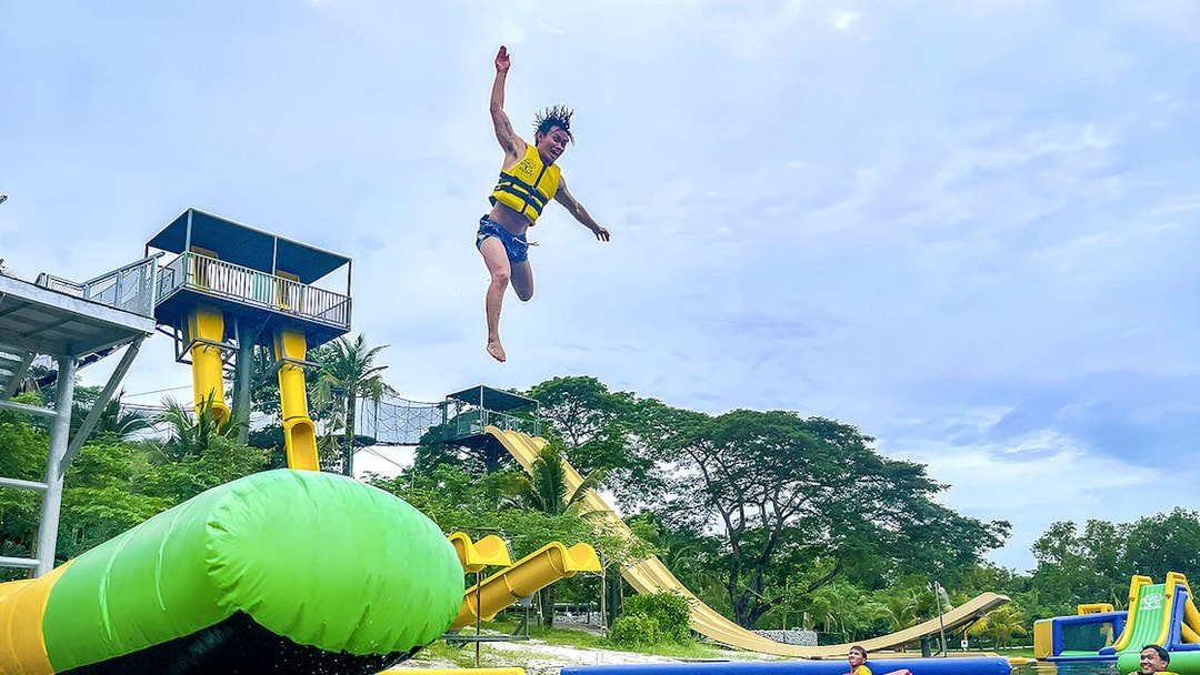 Person jumping from platform at ESCAPE Ipoh Theme Park with water slides and inflatable structures.