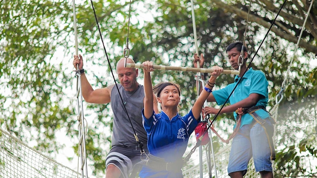 Woman on trapeze at Escape Penang with instructors assisting.