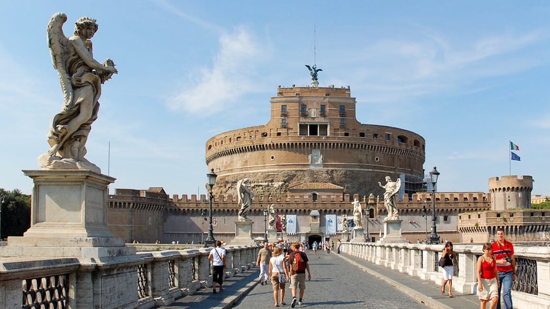 Tour group walking towards Castel Sant'Angelo in Rome, Italy, with historic statues and architecture.