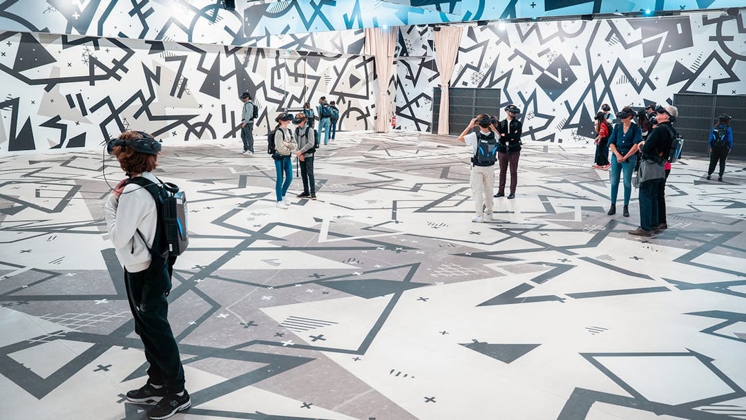 Visitors wearing VR headsets in a geometric-patterned room for the Eternal Notre-Dame VR Experience.