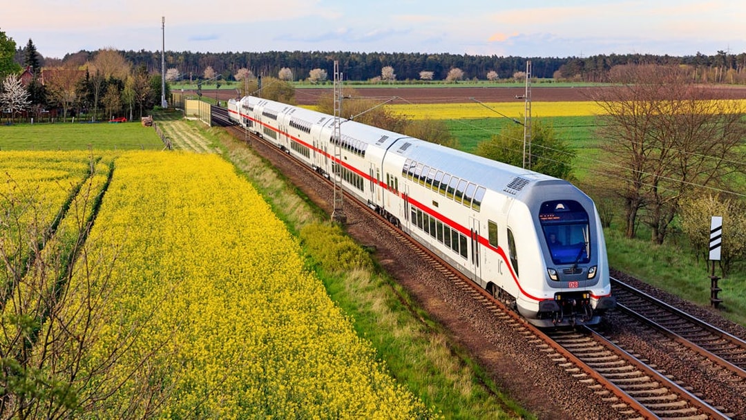 Intercity train traveling through rural Germany with fields and trees in the background.