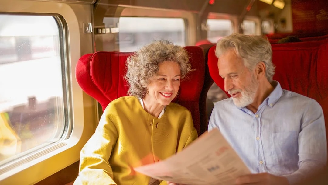Couple enjoying Eurail Global Pass 1st class seats on a scenic train journey.