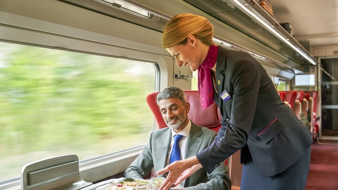 Crew serving meal to first class passenger on a train journey.