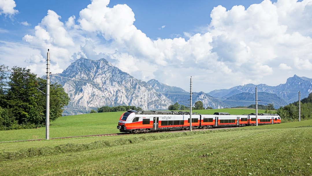 Train traveling through scenic European countryside with mountains in the background.