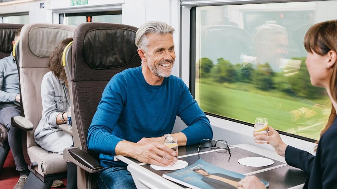 Travelers enjoying drinks in first-class seats on a Eurail train.