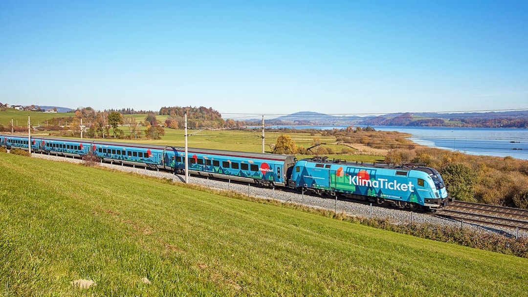 Train traveling through scenic countryside near a lake, promoting KlimaTicket.