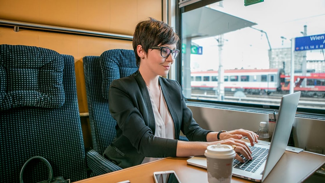 Professional woman working on laptop in first class train seat, Vienna station visible outside.