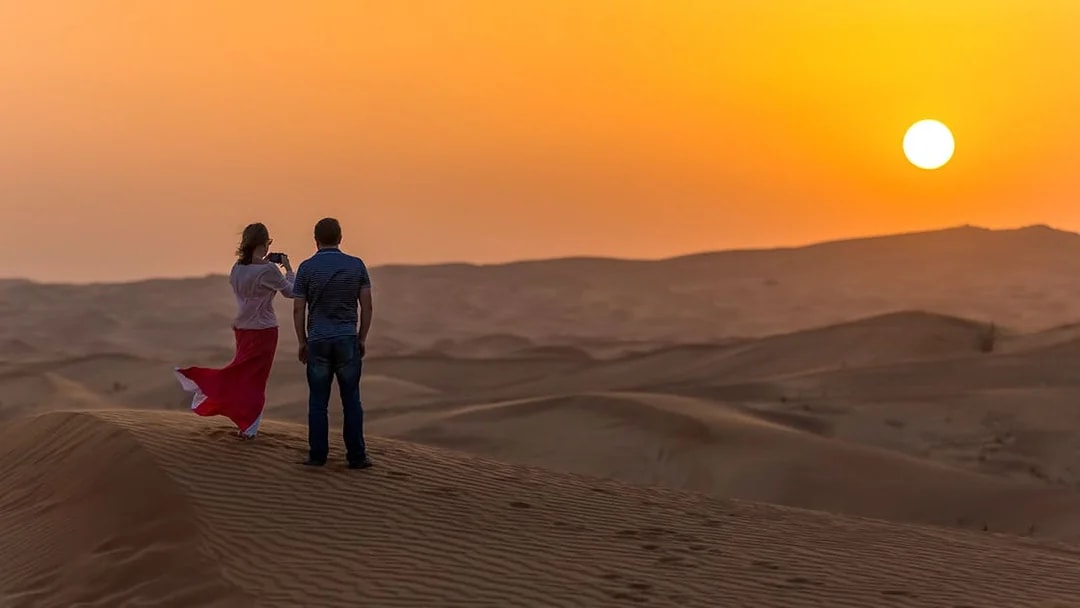 Couple watching sunset over desert dunes during evening safari in Dubai.