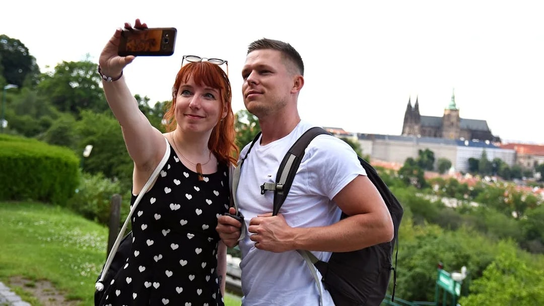 Couple taking a selfie with Prague Castle in the background during an evening walk.