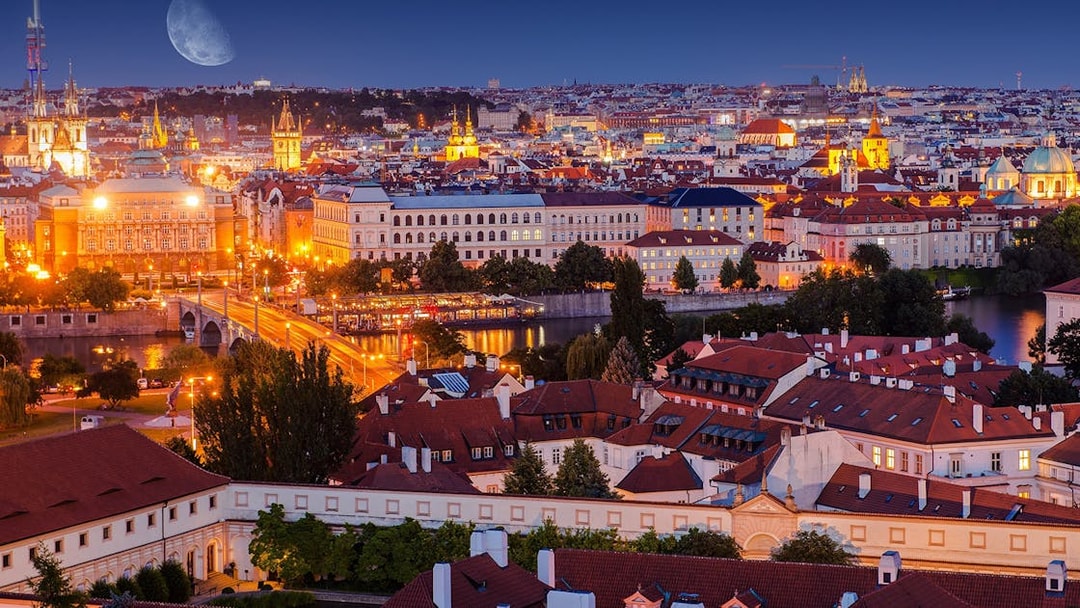Evening view of Prague cityscape with illuminated buildings and Vltava River.