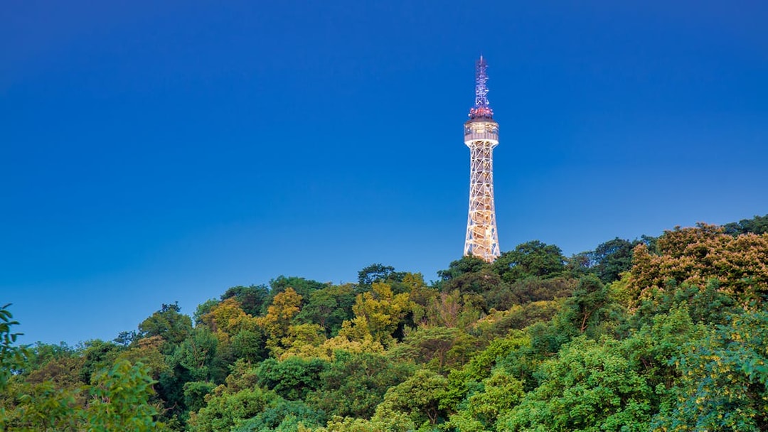 Lit Petřín Lookout Tower above green trees during evening walk in Prague.