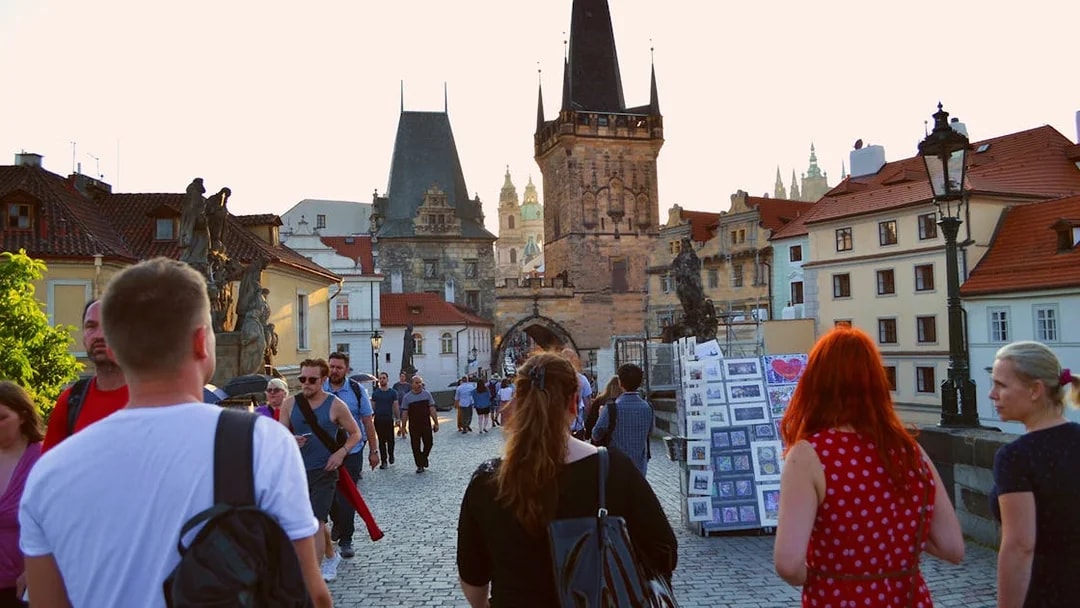 Evening walk on Charles Bridge, Prague, with view of Gothic towers and street vendors.
