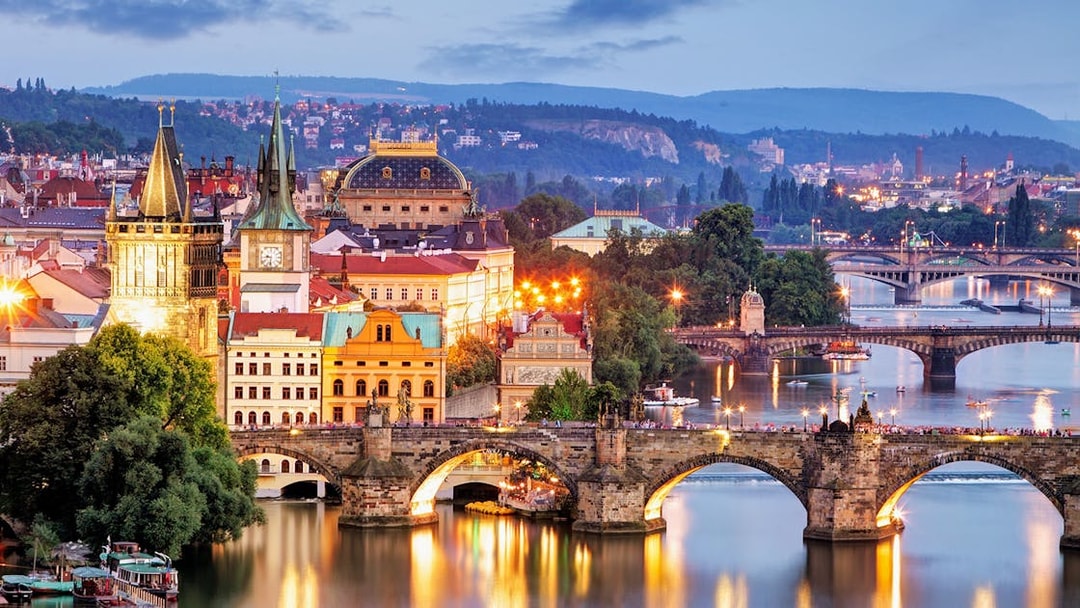 Evening view of Charles Bridge and Vltava River in Prague with illuminated cityscape.