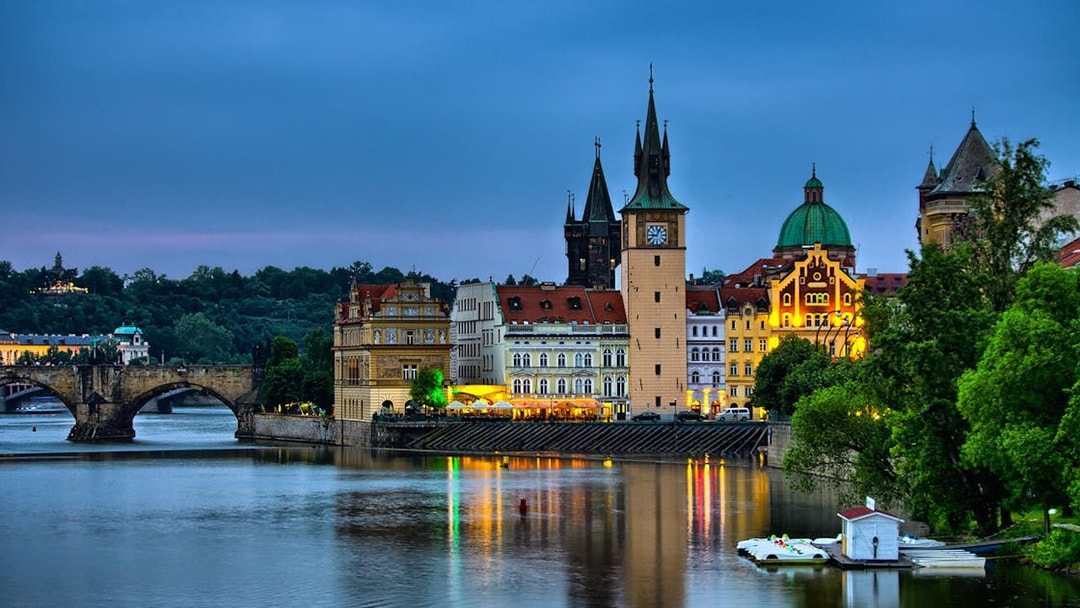 Evening view of Prague's Charles Bridge and Old Town buildings reflecting on the Vltava River.