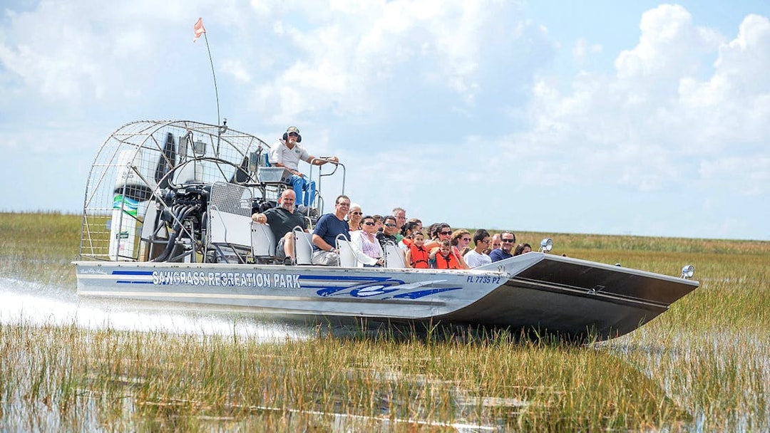 Airboat with tourists gliding through Everglades marshland at Sawgrass Recreation Park.