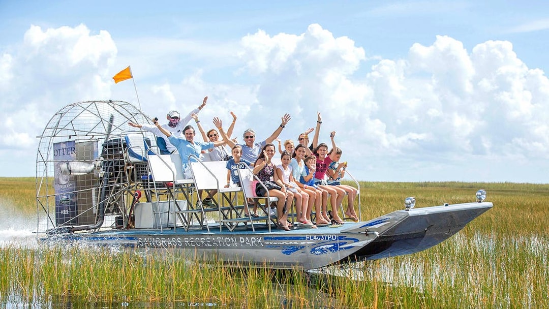 Group enjoying an airboat ride through the Everglades with grassy wetlands in the background.