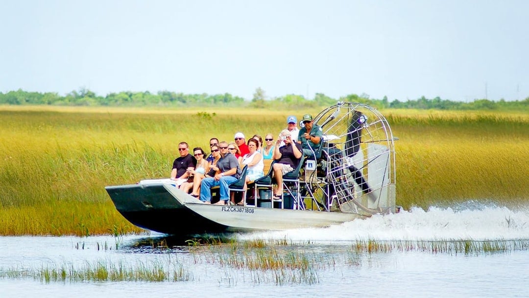 Airboat with tourists gliding through Everglades National Park wetlands.