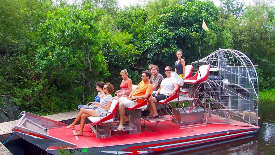 Tourists seated on an airboat in Everglades National Park, surrounded by lush greenery.