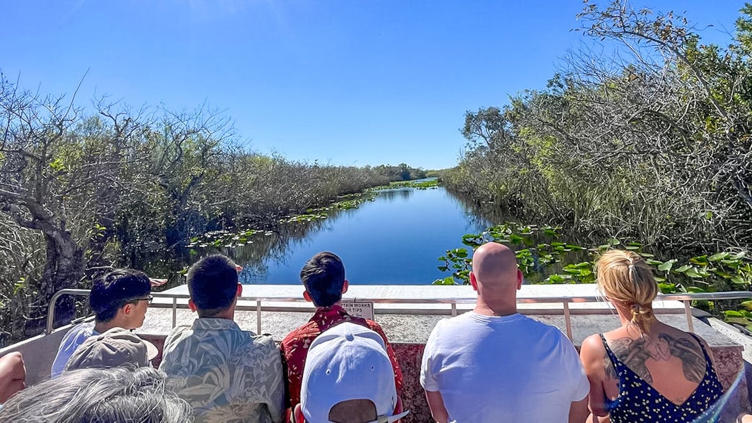 Tourists on an airboat in Everglades National Park, Miami, surrounded by water and vegetation.