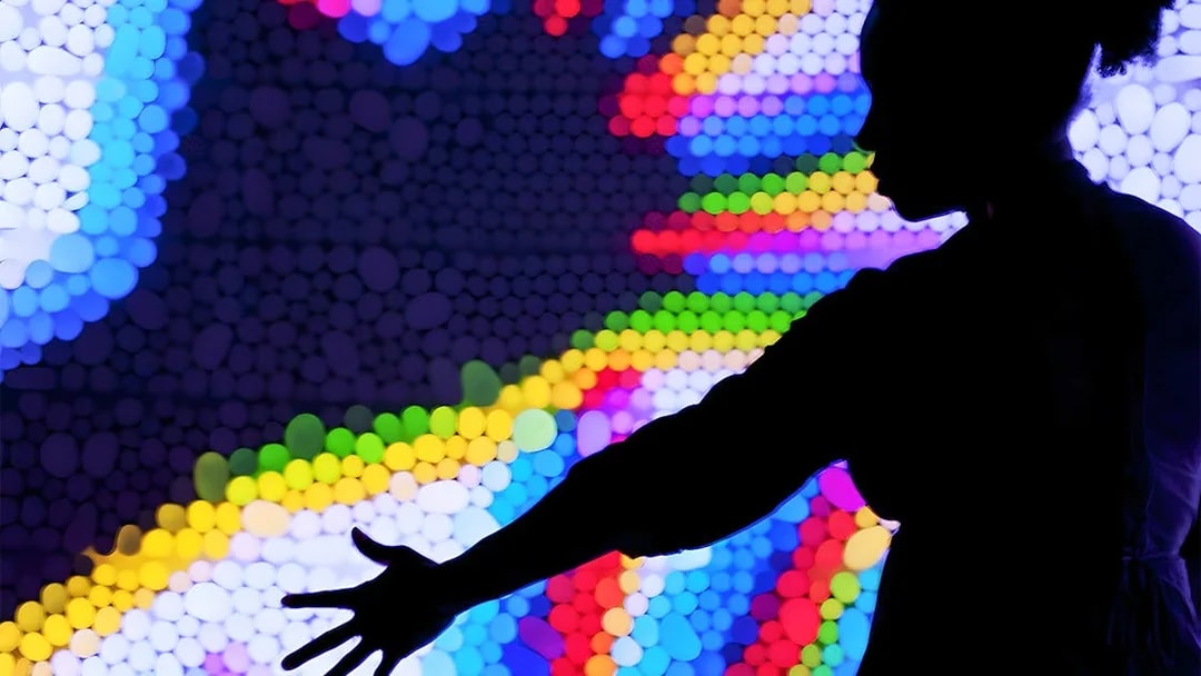 Silhouette of a person reaching towards colorful light display at the Exploratorium.