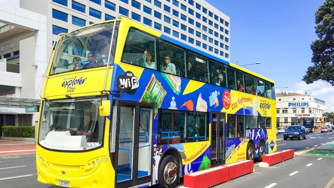 Auckland Explorer Bus at Viaduct Harbour with city skyline in background.