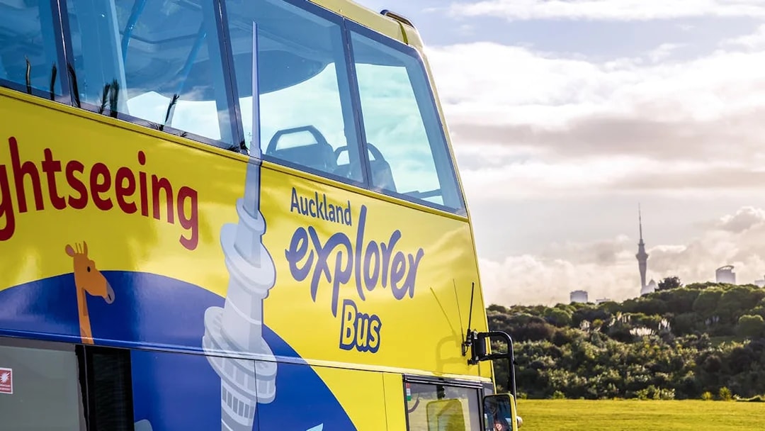 Auckland Explorer Bus with Sky Tower in the background on a city tour.