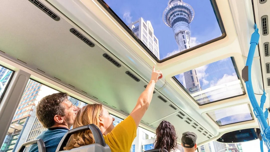 Auckland Explorer Bus passengers view Sky Tower through glass roof.