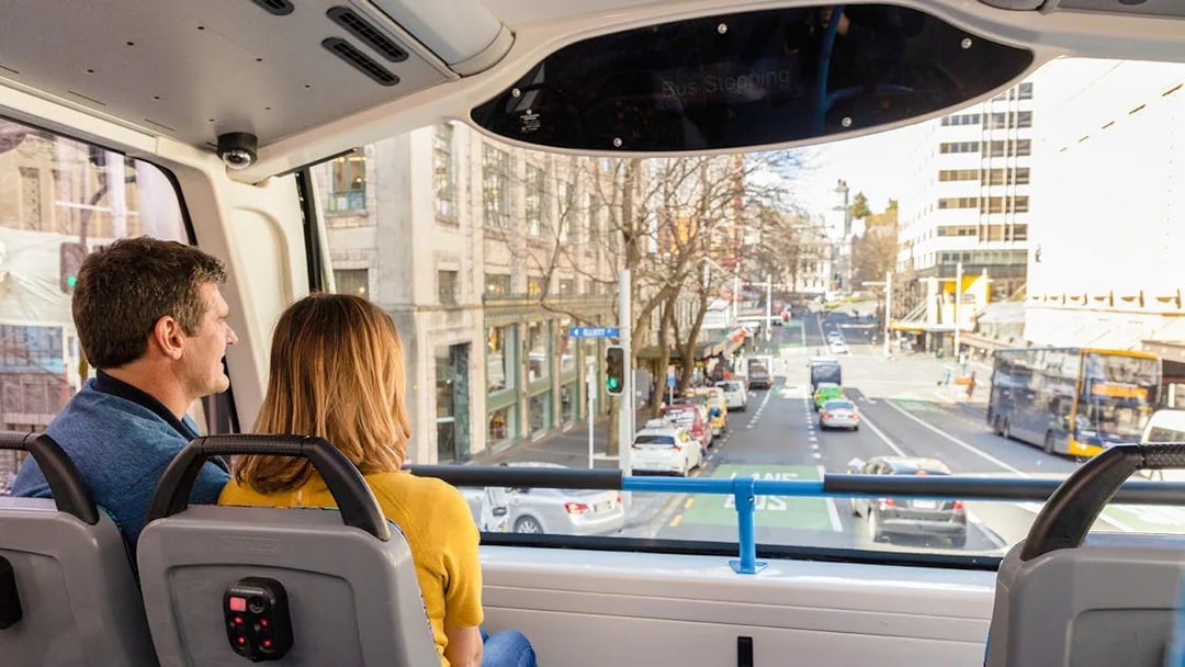 Passengers on Auckland Explorer Bus viewing city street.