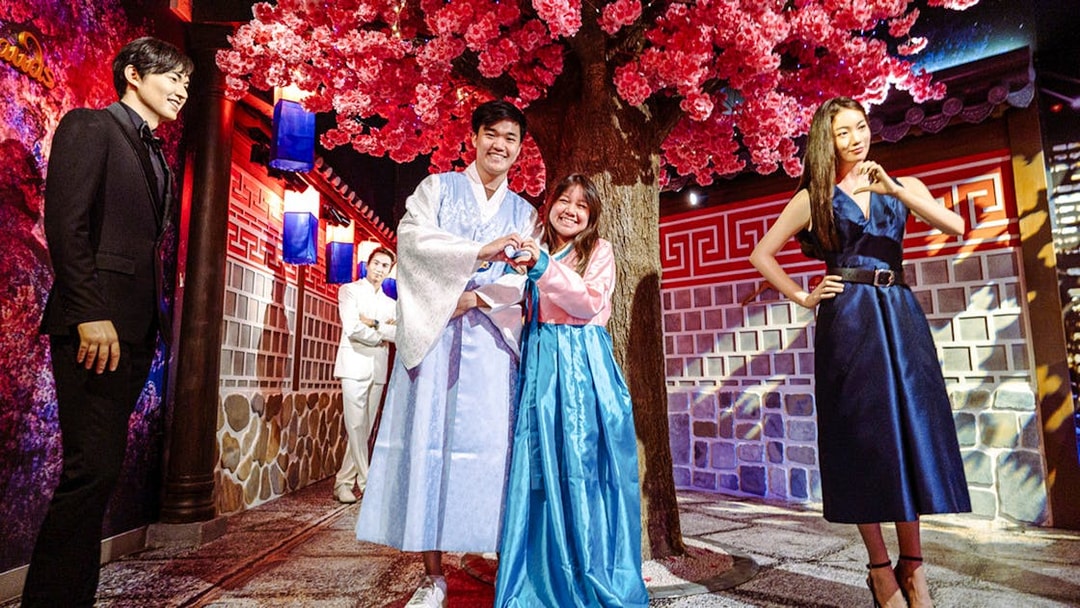 Couple posing in traditional attire at Madame Tussauds Singapore under cherry blossoms.