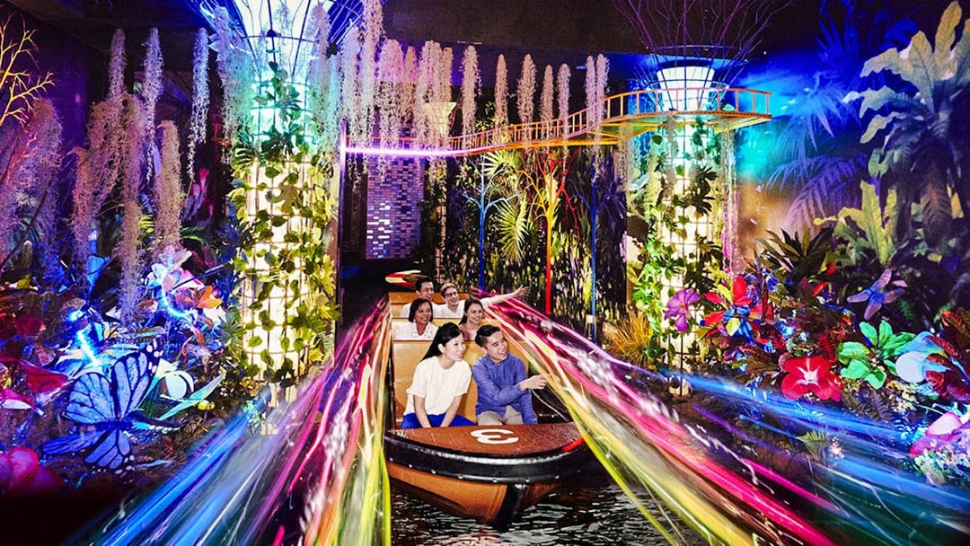 Visitors on a boat ride through vibrant, illuminated gardens at Madame Tussauds Singapore.