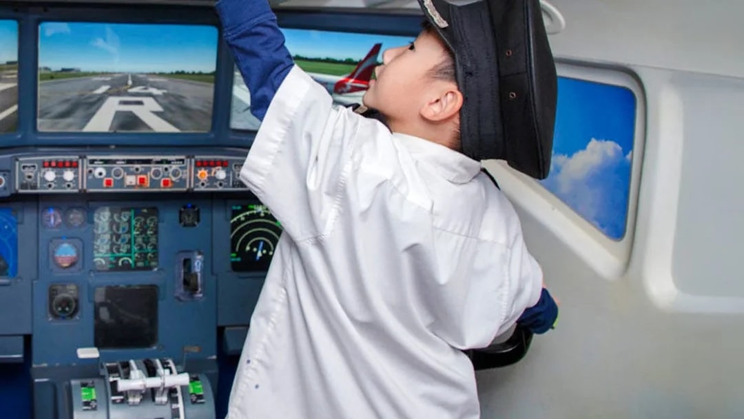 Child in pilot uniform exploring airplane cockpit at KidZania Singapore.