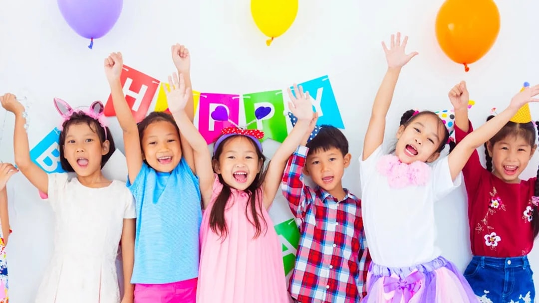 Children celebrating at KidZania with colorful balloons and a birthday banner.