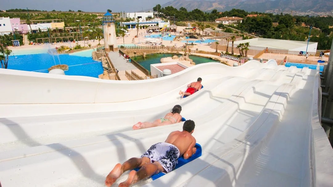 Visitors sliding down water slides at Terra Natura Benidorm with pools and landscape in view.