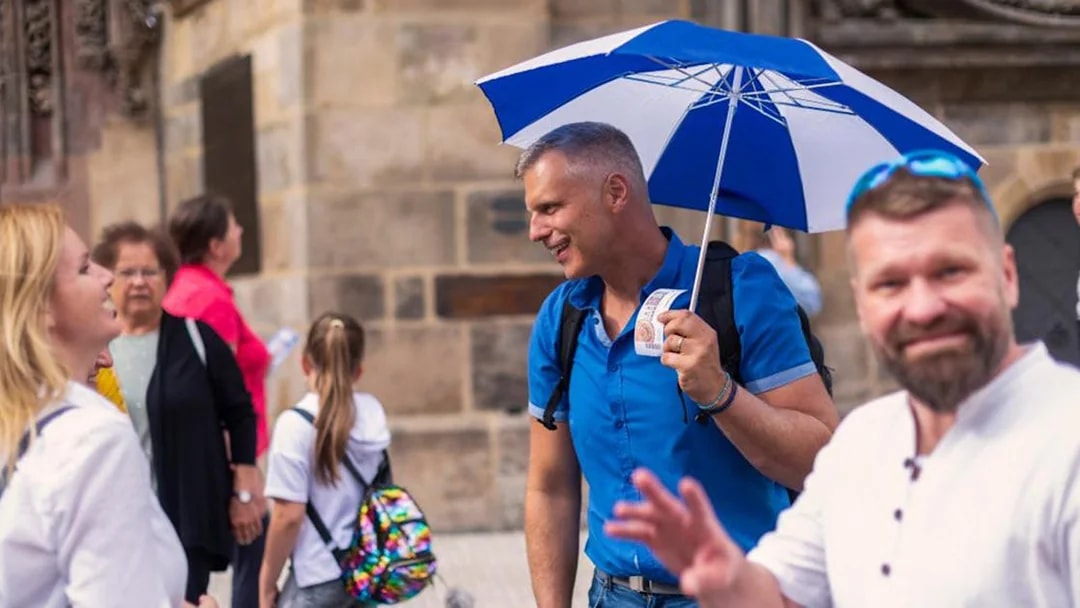 Tourists with guide at Prague Castle entrance, holding tickets and umbrella.