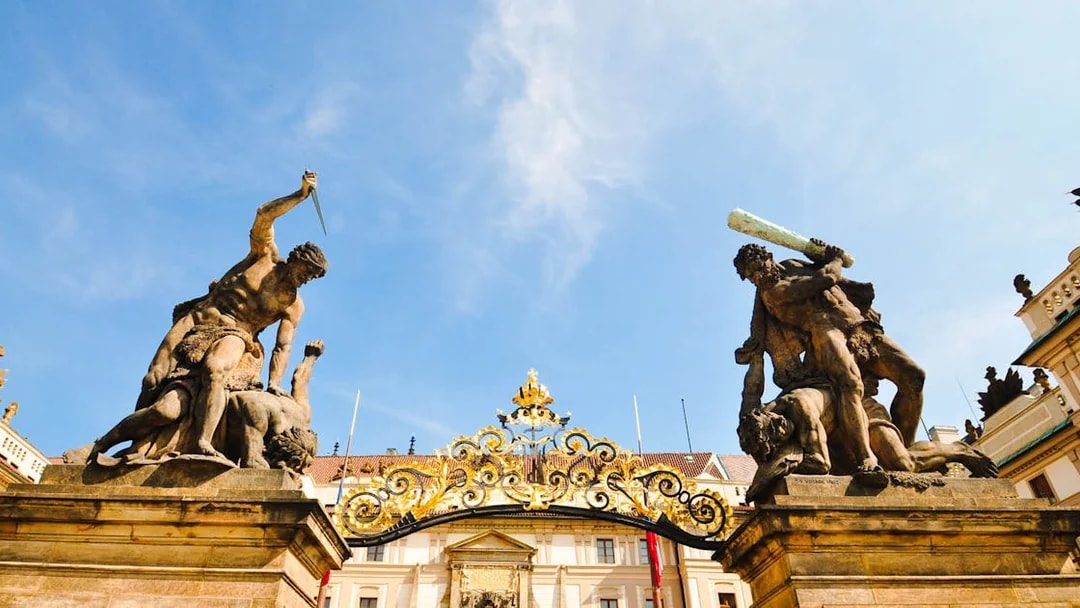 Prague Castle entrance statues with ornate gate under blue sky.