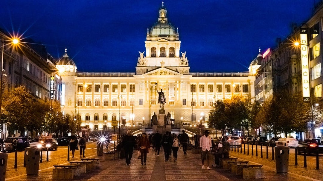 Prague National Museum illuminated at night with people walking in front.