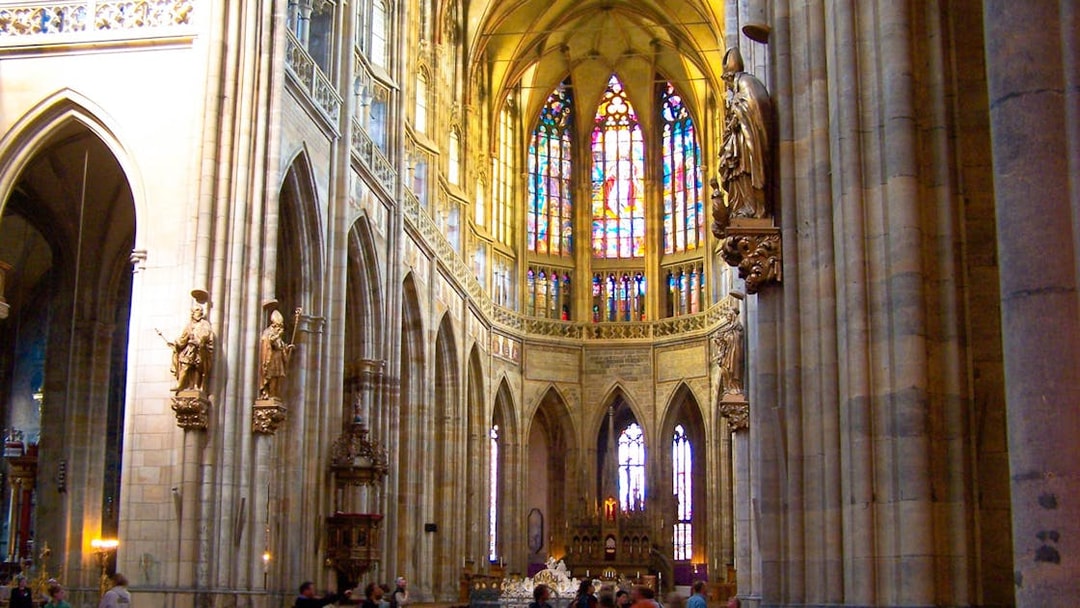 Interior of St. Vitus Cathedral in Prague Castle with stained glass windows and statues.