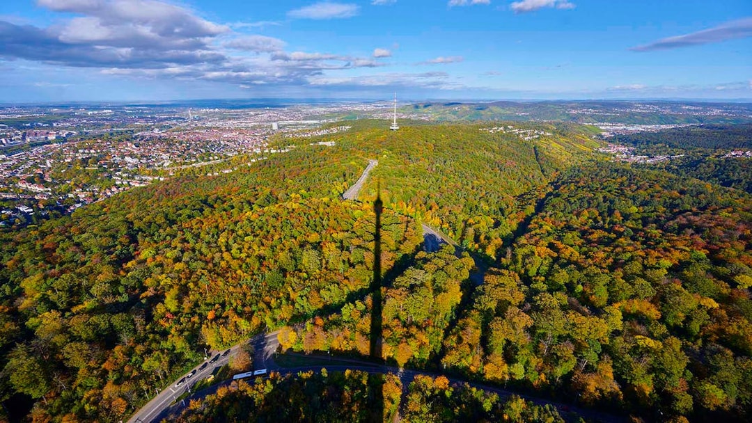 Aerial view of Stuttgart with Fernsehturm shadow over forested hills.