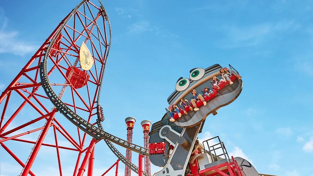 Roller coaster with riders at Ferrari Land, featuring a red track and blue sky.