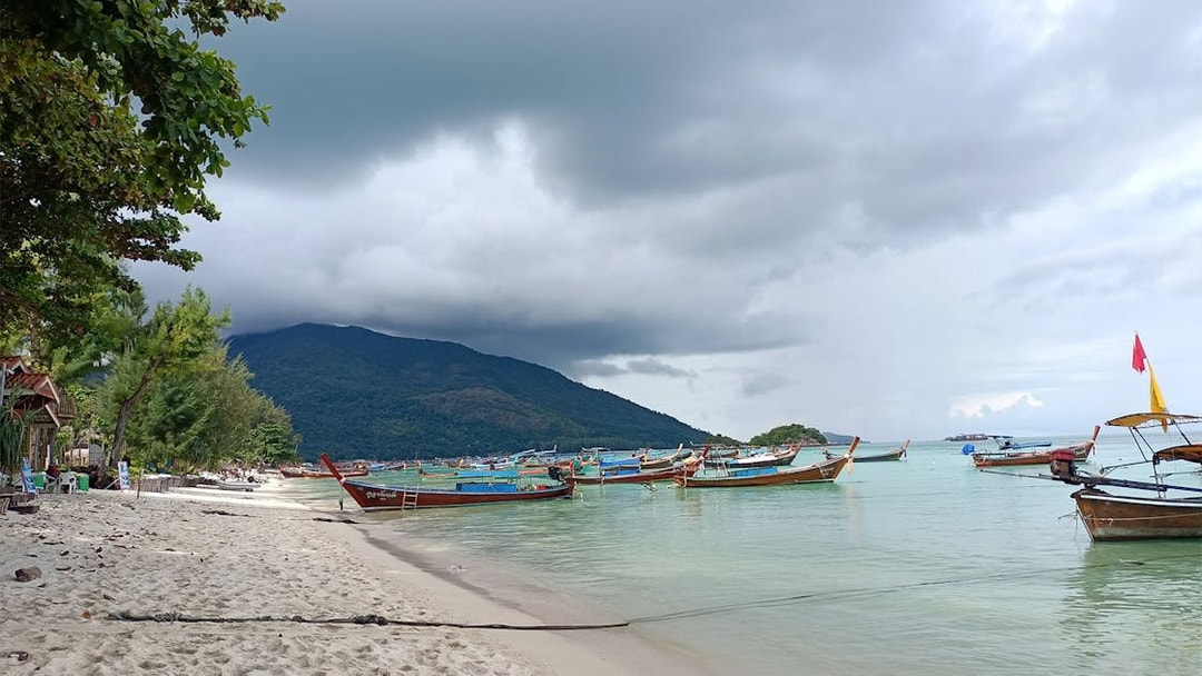 Boats anchored near the shore of Koh Lipe with lush hills in the background.