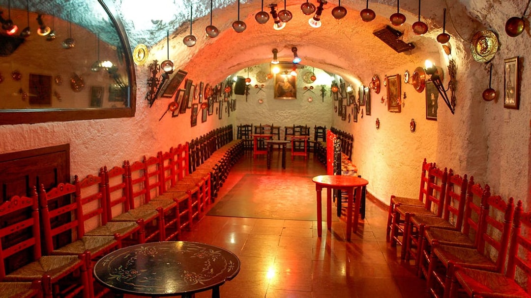 Flamenco Cuevas Los Tarantos performance area with red chairs and rustic decor.