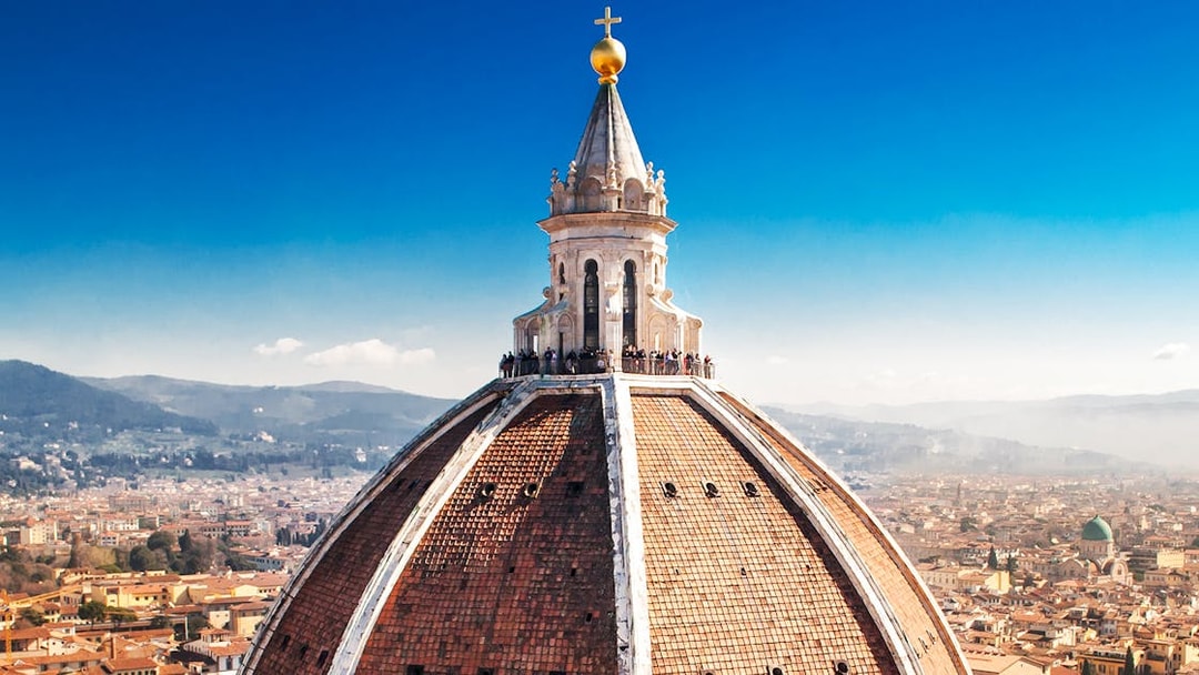 Florence Duomo dome with visitors on secret terraces, cityscape in background.