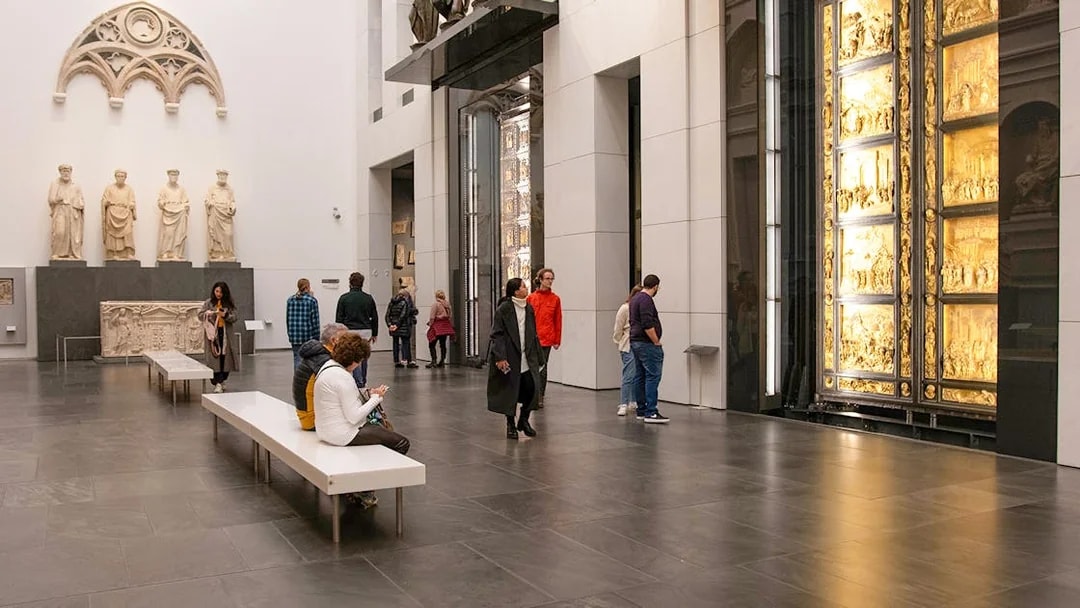 Visitors inside Florence Duomo museum viewing sculptures and the Gates of Paradise.
