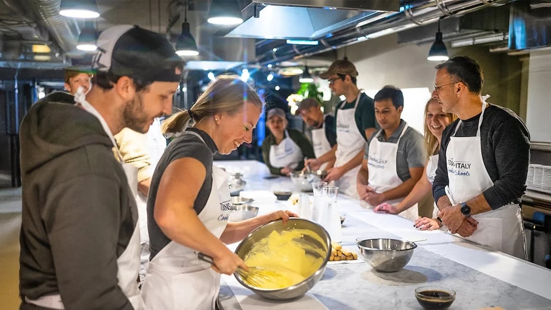 Participants in a Florence pasta-making class whisking ingredients at a kitchen counter.